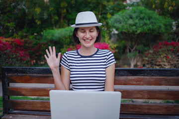 Fototapeta premium woman looking for a job with a laptop in a city park in the summer, Education online. Happy woman calling on laptop, talk by webcam, video conference.
