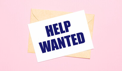 On a light pink background - a craft envelope. It has a white sheet of paper that says HELP WANTED