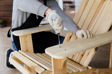 Professional carpenter assembling wooden adirondack chair with screwdriver. Manual work and...