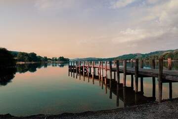 Sunrise over Coniston Water with beautiful pink colours washing over a wooden pier, reflected on the surface of the lake