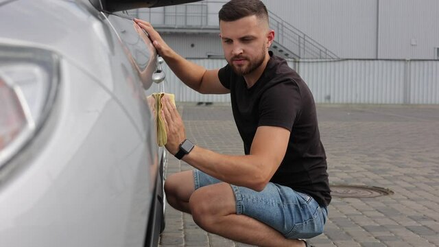 Handsome man wipes a car with a rag in a showroom at a self-service car wash. Gray car