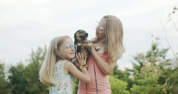 Happy little girls playing with dog in the park and having fun sisters together