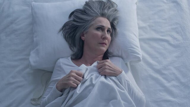 Thoughtful mature woman lying in bed, bad memories at night, anxiety problem