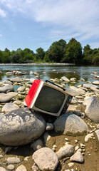Old red Television abandoned on a river stone out of date and without emission