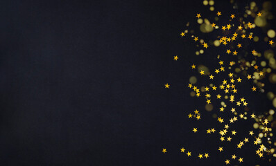 Golden glitter stars confetti on black background with soft golden bokeh