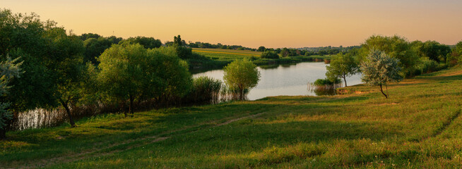 Fototapeta na wymiar Rural landscape, panorama, banner - small country lake with a meadow and green forest in the background