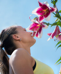 Young woman is smelling a lily flower on blue sky background.