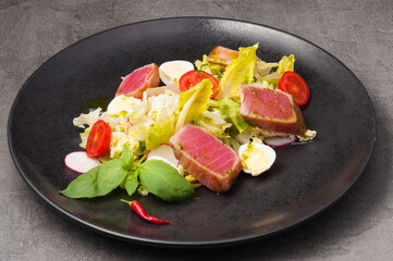 salad with fried tuna, vegetables and quail egg on a black plate