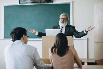 Back view. Elderly gray-headed man, professor, teacher and students at lecture, lesson at classroom, indoors. Concept of professional occupation, job, education