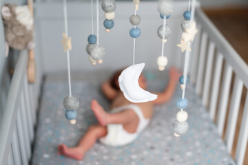 Baby crib mobile with stars, planets and moon hang over the sleeping newborn. Kids handmade toys above the newborn crib. First baby eco-friendly toys made from felt and wood