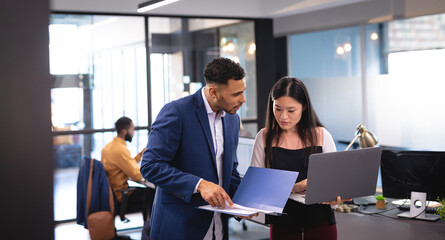 Two diverse male and female business colleagues using laptop and talking