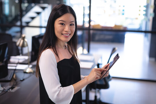 Portrait of smiling asian businesswoman using tablet and looking at camera