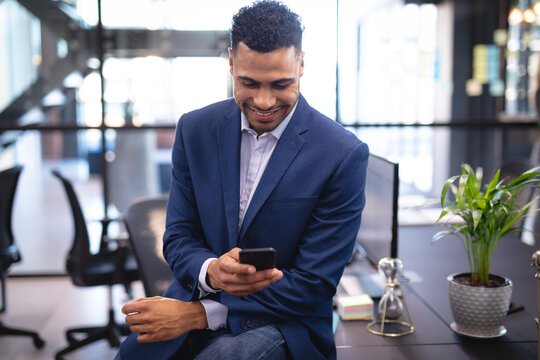 Mixed race businessman using smartphone and sitting at desk