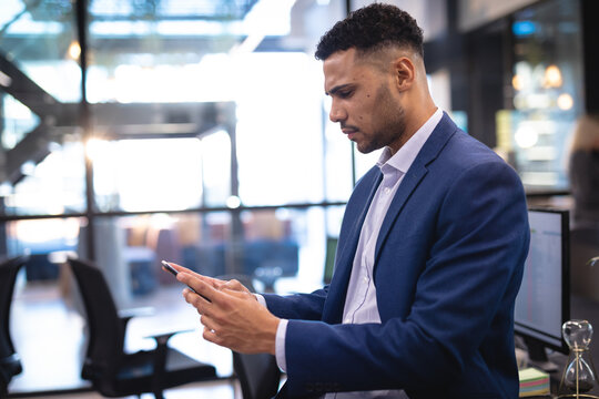 Mixed race businessman using smartphone and sitting at desk