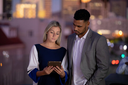 Diverse male and female business colleagues working at night using tablet and talking