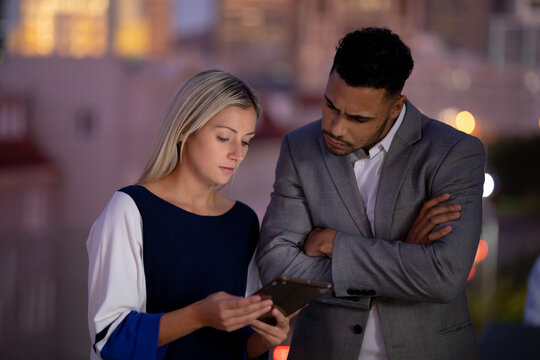 Diverse male and female business colleagues working at night using tablet and talking