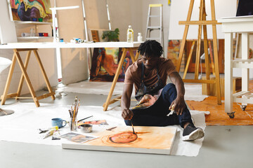 African american male painter at work painting portrait on canvas in art studio