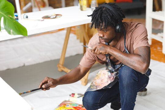 African american male painter at work painting portrait on canvas in art studio