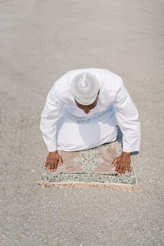 Islamic man praying on mat on beach