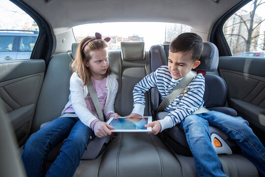 Brother and sister fighting over digital tablet on the back seat of the car