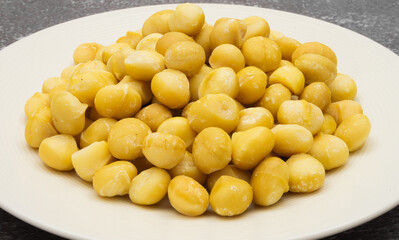 Raw macadamia seeds on plate on stone background