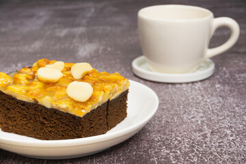 Toffee chocolate cake slice with macadamia seeds at above for dessert break and coffee cup on stone background