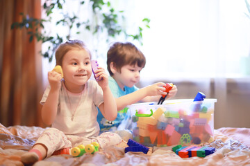 Children play construction set sitting on the sofa and watch cartoons on TV.
