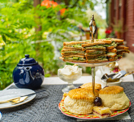 traditional English cream tea with scones and cucumber sandwiches in a garden patio
