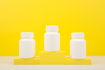 Creative composition with three white medication bottles on winner pedestal against bright yellow background with copy space. Concept of citrus vitamins or vitamins for kids or pharmaceutical industry