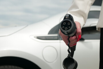 Female hand shows socket type 1. Business woman holding an electric car plug on background of EV. Eco friendly alternative energy green environment concept