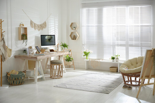 Stylish home office interior with comfortable workplace and papasan chair
