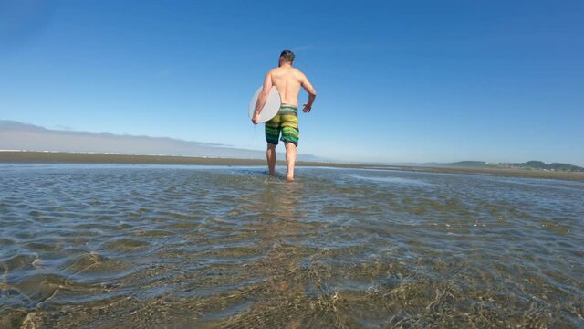 Man Holding Skim Board Walking Slow Motion in Tide Pool on Sandy Beach