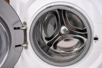 Front-loading washing machine in laundry room, the washing machine lid is opening, visible inside the drum.