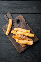 Churros with sugar and chocolate sauce, on black wooden table background, top view flat lay