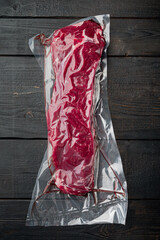 Sirloin beef steak in vacuum packaging. Market pack, on black wooden table background, top view...