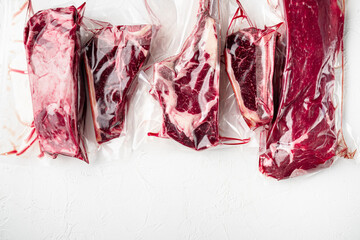 Vacuum packed organic raw beef classic cuts, tomahawk, t bone, club steak, rib eye and tenderloin cuts, on white stone  background, top view flat lay, with copy space for text - obrazy, fototapety, plakaty