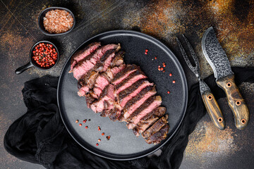 Grilled or fried and sliced marbled meat steak rib eye, on plate, with meat knife and fork, on old...