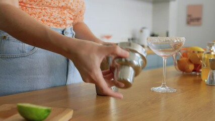 drinks and people concept - young woman with shaker making cocktail at home kitchen
