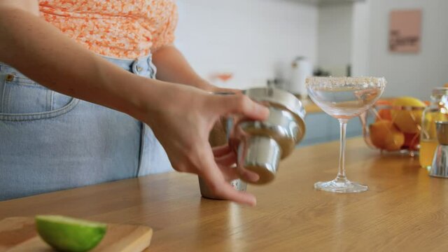 drinks and people concept - young woman with shaker making cocktail at home kitchen
