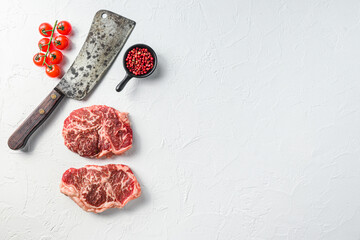 Raw top blade steak, organic meat with seasonings and butcher cleaver. White textured background. Top view with space for text.