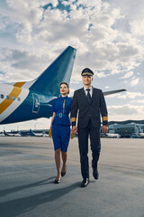 Smiling female flight attendant and an airplane pilot going ahead - obrazy, fototapety, plakaty