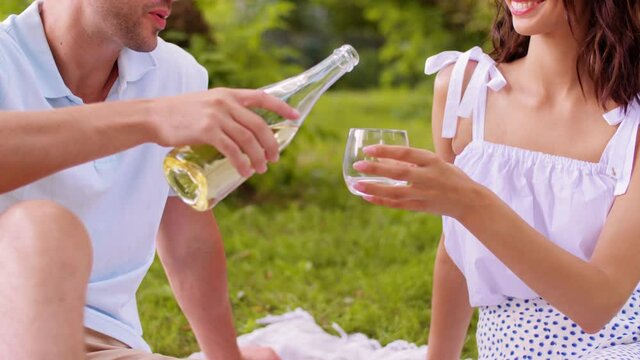 leisure and people concept - happy couple having picnic and pouring wine to glass at summer park