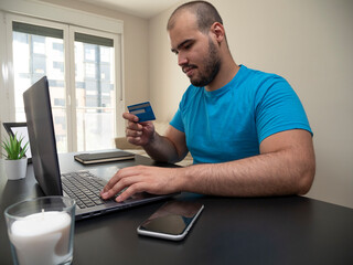 Young man working from his living room on a laptop on a black table with a white candle his phone and a credit card with a black notebook