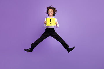 Fototapeta na wymiar Full size photo of funny little brunet boy jump hold sign wear shirt trousers sneakers isolated on purple color background