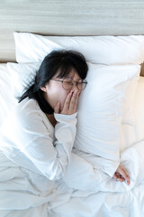Glasses Asian woman are yawning after waked up on the bed in the morning time.