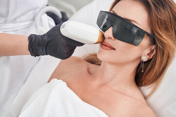 Relaxed pretty woman during face laser epilation - obrazy, fototapety, plakaty