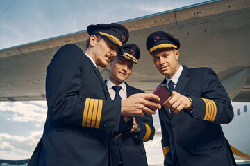 Male pilot demonstrating the content of his cellphone to his friends - obrazy, fototapety, plakaty