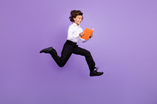 Full size photo of nice little brunet boy jump read book wear shirt trousers sneakers isolated on purple color background