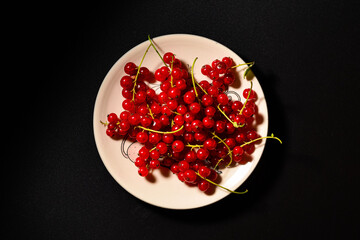 red currant berries on a plate top view. black background with red currant.