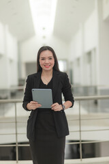 Happy and smiling Asian businesswoman in black business dress using digital tablet working in an office building.